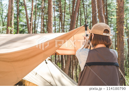 キャンプでテント・タープの設営を手伝う女性キャンパーの後姿 キャンプでテント・タープの設営を手伝う女性キャンパーの後姿 114180790