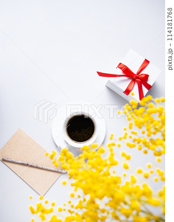 a spring bouquet with yellow mimosa flowers over a cup of black coffee, present box a spring bouquet with yellow mimosa flowers over a cup of black coffee, present box 114181768