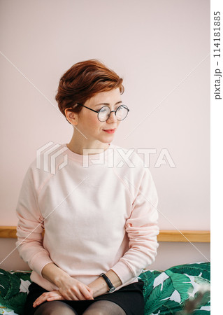 Portrait of middle-aged woman wearing eyeglasses on pink background in home Portrait of middle-aged woman wearing eyeglasses on pink background in home 114181885