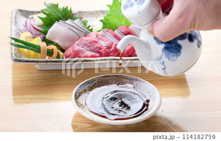 鯨のお刺身盛り合わせをバックにお醤油を注ぐ 114182759