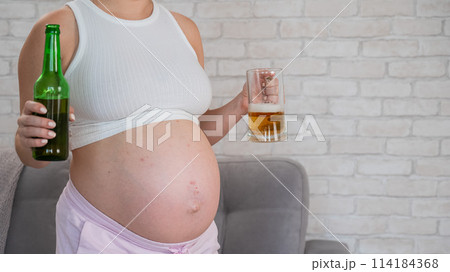 Pregnant woman holding glass and bottle of beer. Pregnant woman holding glass and bottle of beer. 114184368