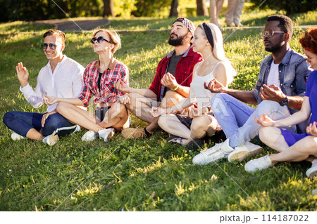 Group of adult friends meditating while practicing yoga outside in park. 114187022