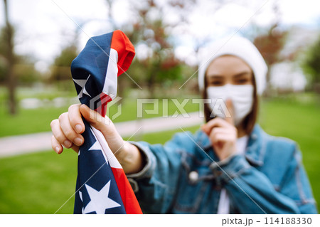 Girl in protective sterile medical mask and with american flag in hand. Quarantine city. Covid -19. 114188330