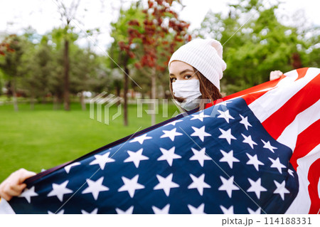 Girl in protective sterile medical mask and with american flag in hand. Quarantine city. Covid -19. 114188331