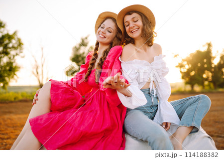 Two smiling young woman resting near haystack. Fashion concept. Nature, vacation, relax and lifestyle. 114188382