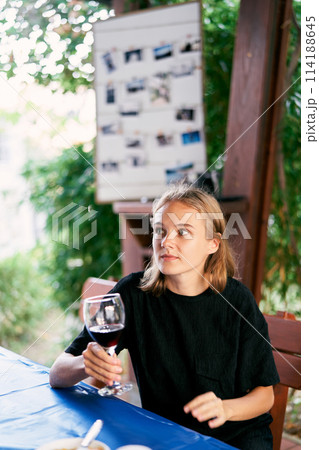 Young woman with a glass of wine in her hand sitting at the table. High quality photo 114188645