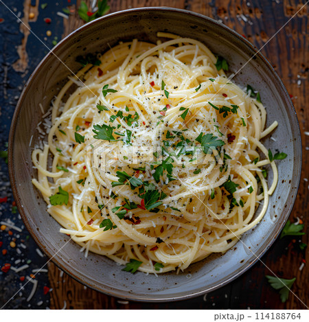 A dish of al dente spaghetti topped with cheese and parsley, served on a wooden table. A staple food in many cuisines made with noodles, a common ingredient in recipes 114188764