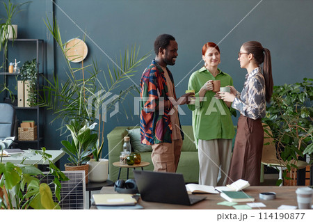 Creative business team of three people communicating standing in modern office at coffee break against blue wall copy space Creative business team of three people communicating standing in modern office at coffee break against blue wall copy space 114190877