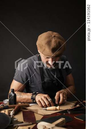 Whiskered shoemaker with making measurments in patterns at table in workshop 114191062
