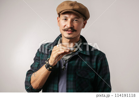Studio portrait of caucasian moustached man on cap playing harmonica 114191118