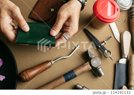 Leather goods master and handmade leather wallets. Workflow in the workshop. Leather goods master and handmade leather wallets. Workflow in the workshop. 114191133