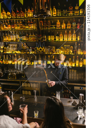 Bartender makes alcoholic drinks pouring orange liquid 114191306