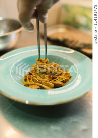 Chef twists noodles around metal chopsticks serving dish Chef twists noodles around metal chopsticks serving dish 114191478