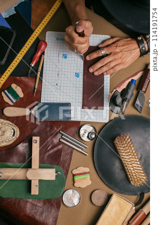 Close up of a shoemaker working with leather textile and hammer at a workshop Close up of a shoemaker working with leather textile and hammer at a workshop 114191754