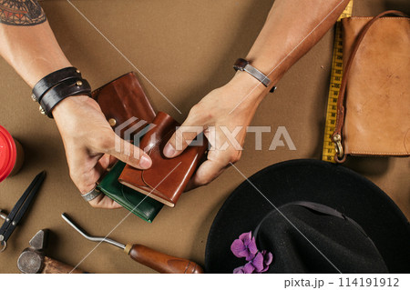 Leather goods master and handmade leather wallets. Workflow in the workshop. Leather goods master and handmade leather wallets. Workflow in the workshop. 114191912