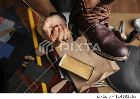 Close up of shoe maker hands producing boots in his leather workshop 114192368