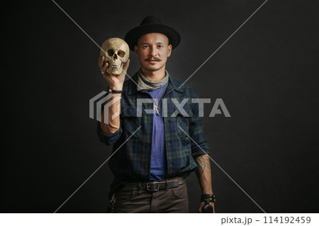 Stylish man with mustache wearing hat and holding scull posing indoors Stylish man with mustache wearing hat and holding scull posing indoors 114192459