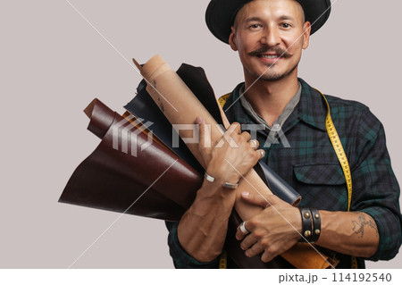 Artisan of leather in creative black hat posing with leather goods in studio. Artisan of leather in creative black hat posing with leather goods in studio. 114192540