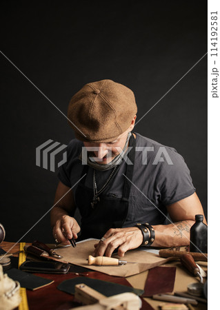 Whiskered shoemaker with making measurments in patterns at table in workshop Whiskered shoemaker with making measurments in patterns at table in workshop 114192581