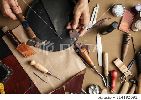 Close up of skinner craftsman working with natural leather using craft tools. Close up of skinner craftsman working with natural leather using craft tools. 114192692