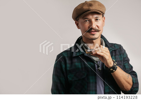 Studio portrait of caucasian moustached man on cap playing harmonica 114193228