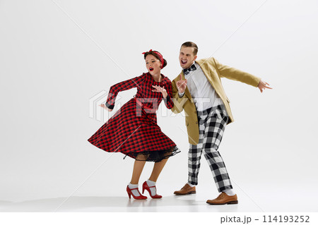 Man in checkered trousers and mustard jacket dancing with woman in red plaid dress playfully dancing isolated over white studio background Man in checkered trousers and mustard jacket dancing with woman in red plaid dress playfully dancing isolated over white studio background 114193252