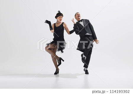 Woman in black flapper dress dancing with man in classic black suit, showcasing lively spirit of the 1920s isolated over white studio background Woman in black flapper dress dancing with man in classic black suit, showcasing lively spirit of the 1920s isolated over white studio background 114193302