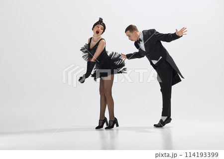 Flirty mood, man and woman in vintage attire engaged in lively dance isolated over white studio background. Roaring twenties Flirty mood, man and woman in vintage attire engaged in lively dance isolated over white studio background. Roaring twenties 114193399