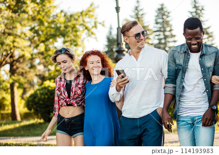 Multi-ethnic group of friends walking and fooling around city park. 114193983