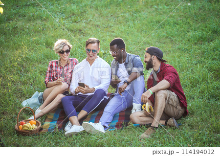Diverse group of cheerful friends sitting on grass at sunset in nature park. Diverse group of cheerful friends sitting on grass at sunset in nature park. 114194012