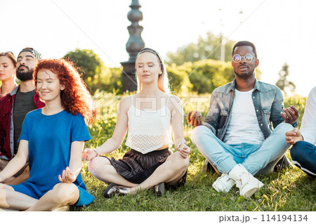 Group of adult mix-race friends meditating while practice yoga outside in park. 114194134