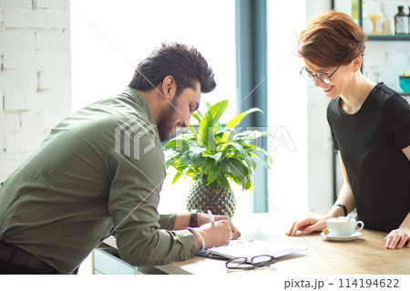 Two business people discuss meeting table with documents and write notes Two business people discuss meeting table with documents and write notes 114194622
