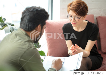 woman is sitting on couch and talking to male indian psychologist while doctor making notes 114194652