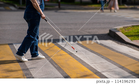 Close-up of the legs of a blind woman crossing the road at a crosswalk with a cane. Close-up of the legs of a blind woman crossing the road at a crosswalk with a cane. 114196293
