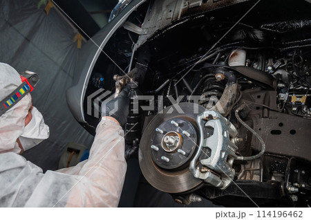 An auto mechanic applies anti-corrosion mastic to the underbody of a car. 114196462