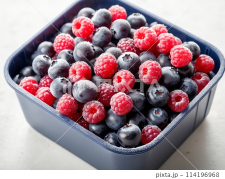 A Berry mix from frozen raspberries and blueberries on the white plate. A Frozen Berries in black background. A sweet background with frozen raspberries and blueberries. 114196968