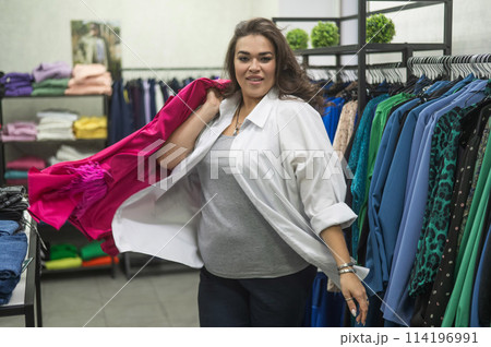 Caucasian fat woman looks excitedly at a festive pink dress in a store. Plus size. Caucasian fat woman looks excitedly at a festive pink dress in a store. Plus size. 114196991