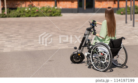 A woman in a wheelchair with an assistive device for manual control. Electric handbike.  114197199