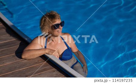 An elderly woman in sunglasses swims in the pool. Vacation in retirement.  114197235