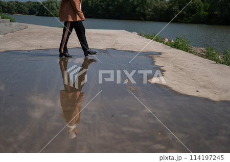 Close-up of a woman's legs walking on a large puddle. Close-up of a woman's legs walking on a large puddle. 114197245