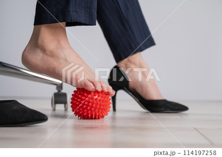 Business woman massages her feet on a massage ball with spikes. 114197258