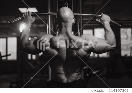 Caucasian man doing lat pull-downs on a machine. Black and white photo.  114197301