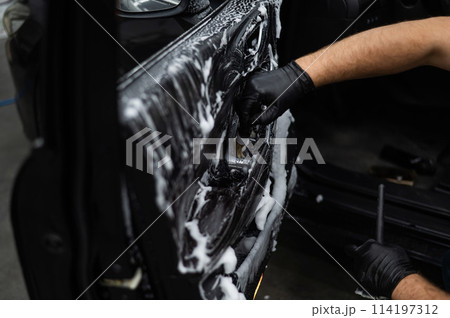 A man cleans the interior of a car with foam and a brush. Clean the door trim. A man cleans the interior of a car with foam and a brush. Clean the door trim. 114197312