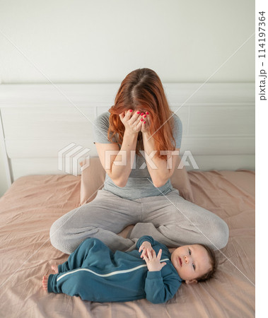 A woman sits on her child's bed and cries. Postpartum depression. Vertical photo. 114197364