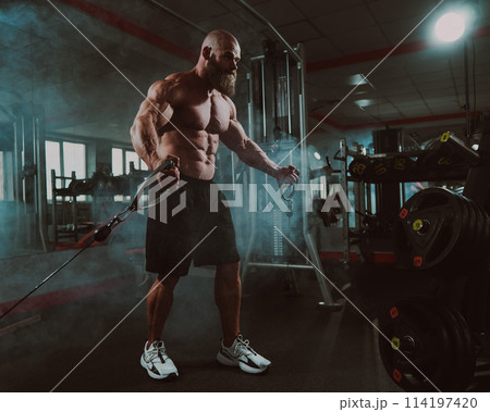 Bald Caucasian bodybuilder training chest using cable crossover in gym. Bald Caucasian bodybuilder training chest using cable crossover in gym. 114197420