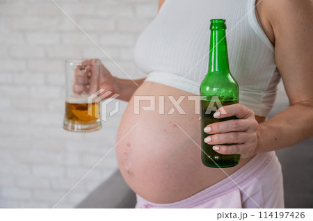 Pregnant woman holding glass and bottle of beer.  114197426