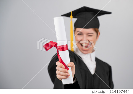 Emotional woman in graduate gown holding diploma in foreground. Emotional woman in graduate gown holding diploma in foreground. 114197444