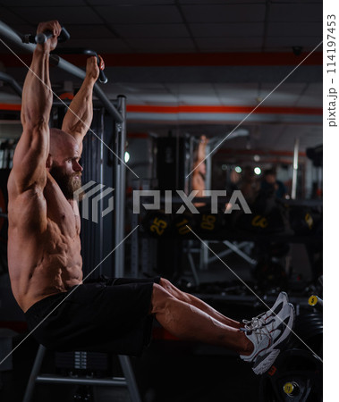 A Caucasian man hangs on a horizontal bar and raises his legs. Vertical photo. A Caucasian man hangs on a horizontal bar and raises his legs. Vertical photo. 114197453