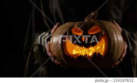 The witch is holding a pumpkin jack o lantern glowing in the dark. Halloween. 114197612