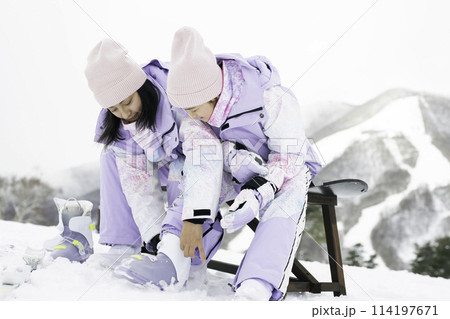 スキー場で娘にブーツを履かせる母親 114197671